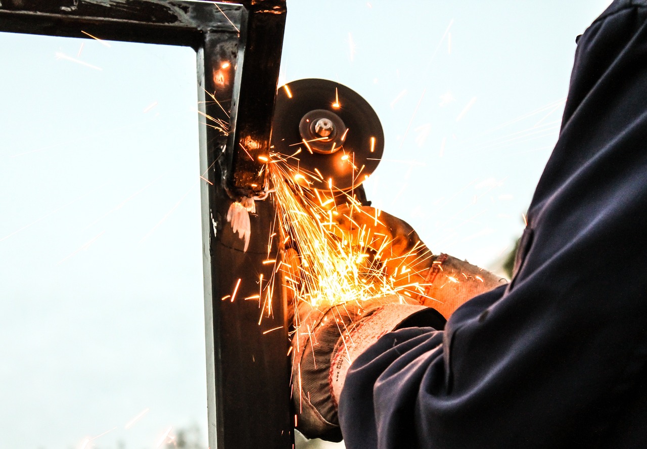 Industrial worker uses angle grinder to cut down steel during a hot summer day